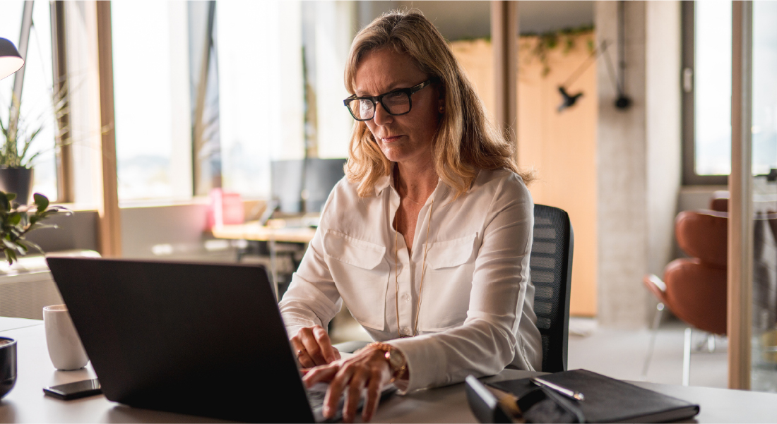 Professional woman in white blouse working on laptop in modern office