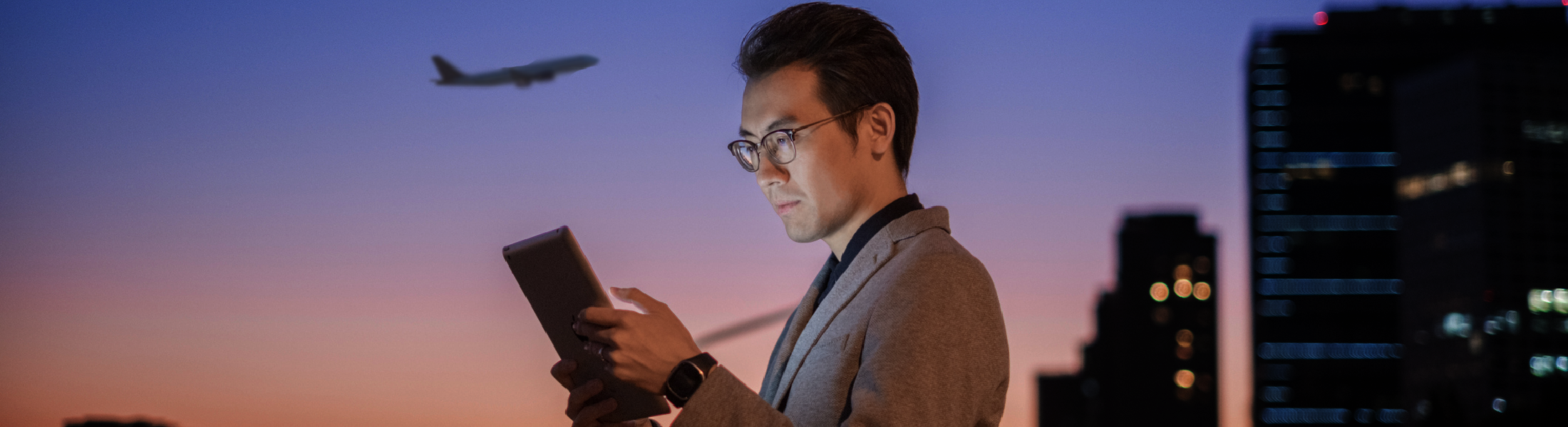 Man using tablet at dusk, plane overhead
