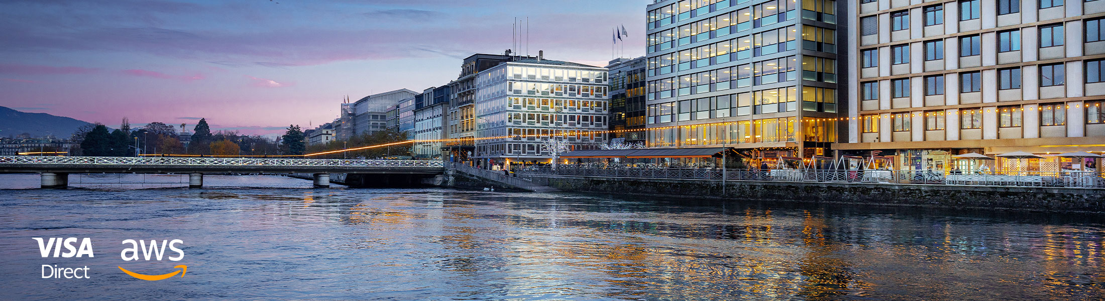 Cityscape at dusk with illuminated buildings and river, featuring Visa Direct and AWS logos.