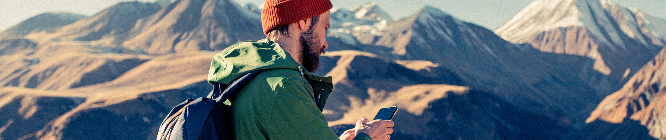 Hiker checks phone with mountains behind