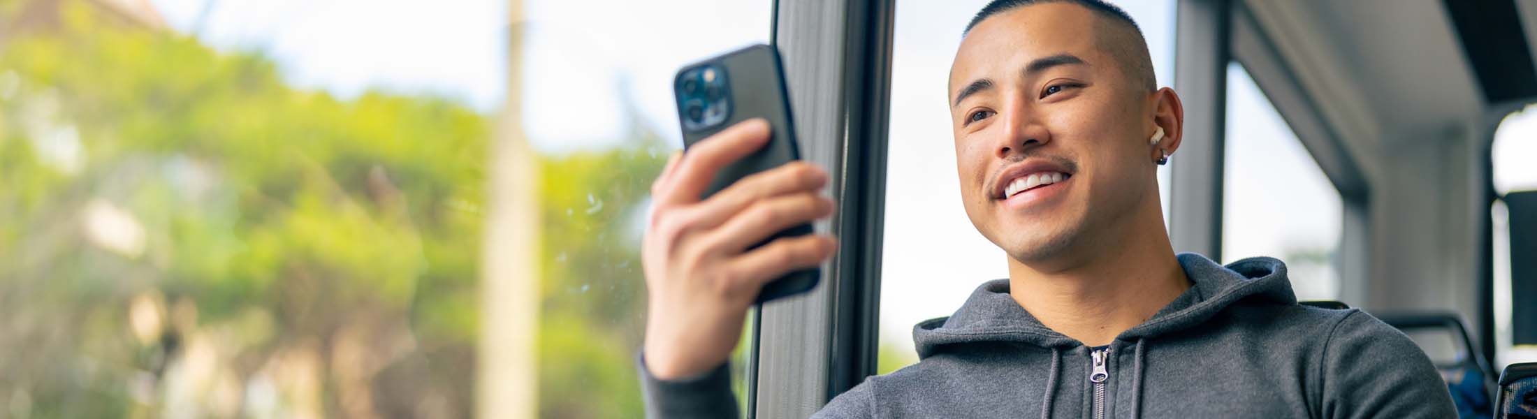 A young man smiling while looking at his smartphone on a bus