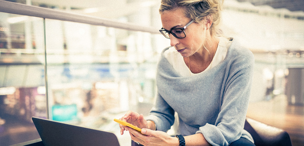 Woman using phone and laptop by window