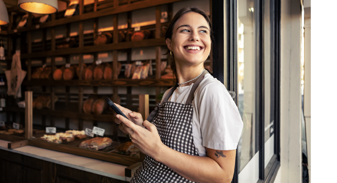 Smiling baker holding phone near bakery window